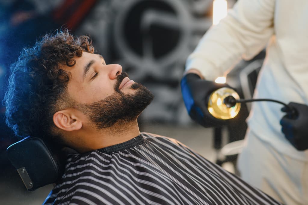 Cliente recostado con los ojos cerrados mientras el barbero le trabaja la barba.